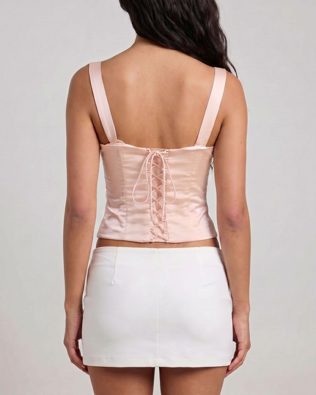 Woman wearing a light pink top and white skirt on a plain background